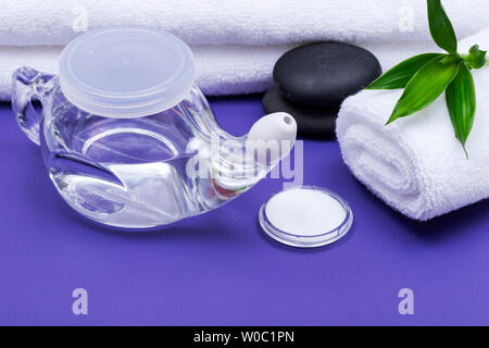 Spa sfondo viola con Neti Pot, pila di soluzione salina, arrotolato Asciugamani Bianchi, impilati pietre di basalto e foglie di bambù. Lavaggio del seno. Irrigazione nasale. Foto Stock