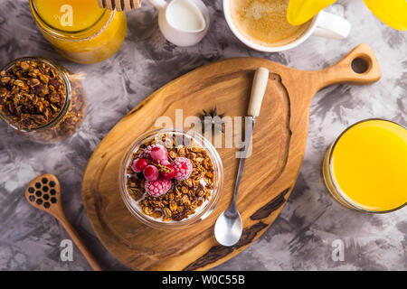 Il dessert con cereali e lo yogurt ho gli acini in bicchieri con doppio vetro per colazione accanto al caffè, fiore e succo di frutta. Vista superiore, laici piatta Foto Stock