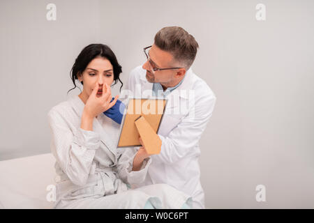 Client del chirurgo di plastica guardando nel retrovisore dopo chirurgia nasale Foto Stock