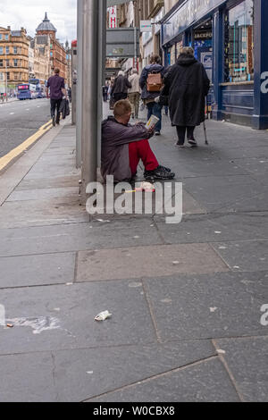 Glasgow, Scotland, Regno Unito - 22 Giugno 2019: le persone camminare davanti a un gentiluomo maschio ubicazione sul pavimento sporco con un McDonald's bicchiere di carta attraente per mon Foto Stock