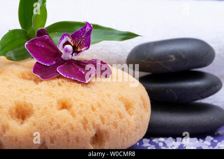 Spa Wellness Concept. Schiuma naturale Bagno & Doccia mare spugna, impilati pietre di basalto, bambù, orchidee e fiori di lavanda Sale di Epsom su sfondo viola Foto Stock