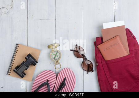 Prepararsi per il viaggio - accessori e articoli da viaggio, imballaggio abbigliamento jeans, passaporti, biglietti, flip-flop, occhiali da sole, Bussola Binocolo su bianco wo Foto Stock