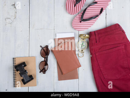 Prepararsi per il viaggio - accessori e articoli da viaggio, imballaggio abbigliamento jeans, passaporti, biglietti, flip-flop, occhiali da sole, Bussola Binocolo su bianco wo Foto Stock