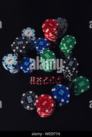 Close up di pile di colore diverso poker chips e riproduzione di dadi sul tavolo del casinò isolate su sfondo nero. Torneo di gioco d'azzardo scommesse per Foto Stock