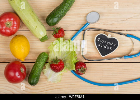 Una buona e sana dieta concetto - Lavagna a forma di cuore con testo indice glicemico, uno stetoscopio, ortaggi e frutta e bacche sul tavolo di legno Foto Stock