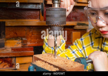 Le donne è permanente di lavoro di artigianato in legno trapano in corrispondenza di un banco di lavoro con drill premere power tools a carpenter la macchina in officina Foto Stock