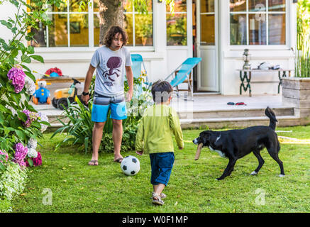 Due ragazzi di 5 anni e 13 anni giocando con una palla in giardino con il loro cane Foto Stock