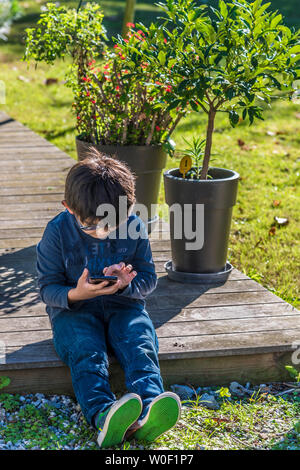 Sette-anno-vecchio ragazzo giocando con un telefono cellulare Foto Stock