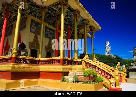 Vista su colonne dorate, il tamburo e il bianco statua di Buddha contro il cielo blu al tempio buddista - Wat Ek Phnom, nei pressi di Battambang, Cambogia Foto Stock