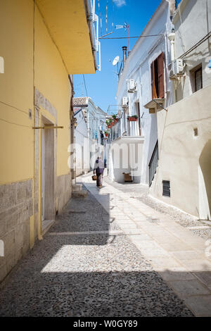 SPINAZZOLA, Italia - 21 agosto 2018: il vecchio uomo cammina verso il basso una pietra strada lastricata che porta un cesto di paglia Foto Stock