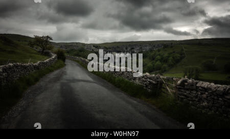 Atmosfera e drammatica hanno colpito la ripida strada fino al lato di Malham Cove in un giorno umido di giugno con un muro di pietra arenaria calcarea, Yorkshire Dales, Regno Unito Foto Stock