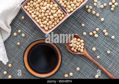 Una piastra di salsa di soia e semi di soia spruzzata su di un tappeto di bambù e in un cucchiaio. Foto Stock