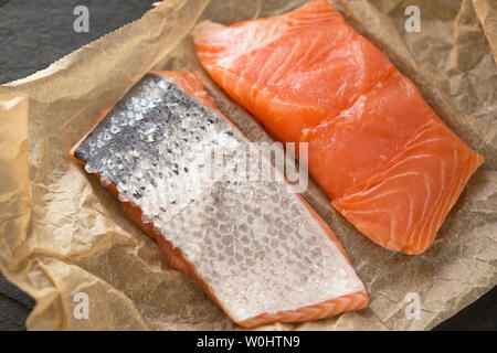 Due filetti di materie di allevamento del salmone scozzese ha acquistato da un supermercato nel Regno Unito che mostra il lato di pelle e il lato carne. Visualizzata sulla cottura marrone pape Foto Stock