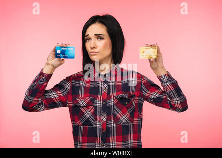 Giovane donna in rosso plaid shirt mostra due carte di credito su sfondo rosa Foto Stock