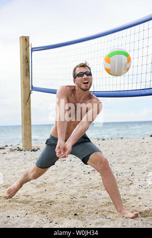 Uomo a giocare a beach volley gioco colpendo avambraccio pass beach volley sulla spiaggia d'estate. Modello maschile sano vivente uno stile di vita attivo facendo sport sulla spiaggia indossando occhiali da sole Foto Stock
