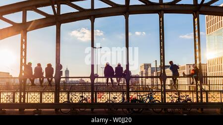 I giovani seduti sulla balaustra del Haccurbrucke ponte sopra i binari ferroviari e guardando in lontananza, luce posteriore, Monaco di Baviera, superiore Foto Stock