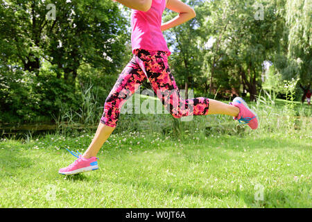 Guida femmina scarpe da corsa e le gambe nel parco della città. Donna jogging indossando floral capris leggings collant a compressione e rosa scarpe da corsa. Foto Stock