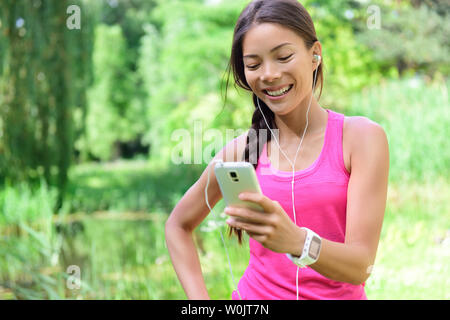 Donna runner di condivisione dei dati in esecuzione sui social media dopo l'esercizio. Ragazza ascoltando musica su smart phone dopo aver eseguito per fare jogging nel parco della città. Pareggiatore femmina con auricolari, smartphone e monitor frequenza cardiaca. Foto Stock