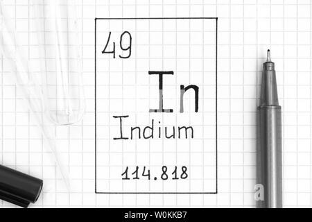 Tavola periodica degli elementi. La grafia elemento chimico indio in con la penna nera, tubo di prova e la pipetta. Close-up. Foto Stock