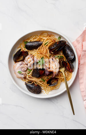 Pasta con frutti di mare e salsa di pomodoro. Spaghetti con il polpo e cozze in bianco ciotola con una forchetta e tovagliolo rosa su sfondo bianco. Concetto di seafoo Foto Stock