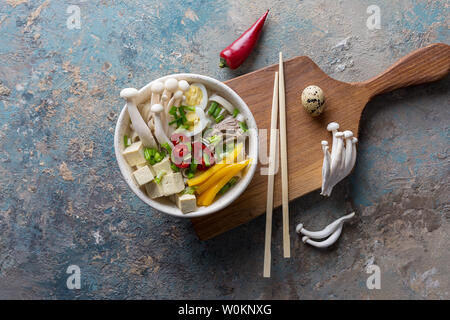 Pasta con funghi e verdure nella ciotola. Peperoncino, peperone giallo, tofu, cipolla, bollito di manzo e funghi cinesi su sfondo di calcestruzzo. Vista superiore f Foto Stock