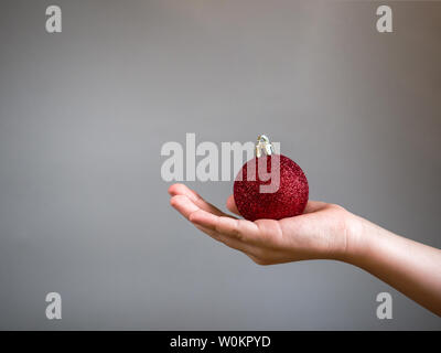 Albero di natale giocattoli come la sfera rossa in mani su sfondo grigio con posto di copia Foto Stock