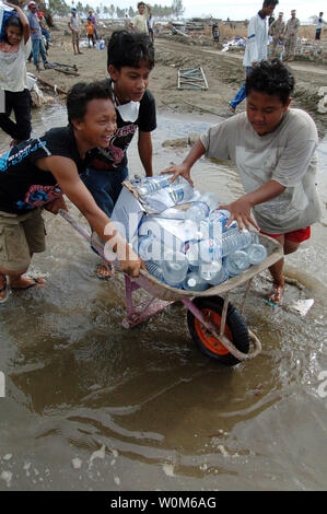 Bambini indonesiano trasportare bottiglie di acqua potabile in una carriola dopo la ricezione da U.S. Marinai e marines che hanno scaricato di forniture di soccorso da una Landing Craft Air Cushion (LCAC) a Meulaboh, Sumatra, Indonesia, a gennaio 11, 2005. (UPI foto/Alan D. Monyelle/Navy US) Foto Stock