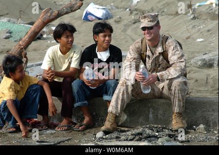 Marine Capt. Jamey Stover, assegnato al XV Marine Expeditionary Unit (MEU), si siede con locali bambini indonesiano come marinai e Marines offload di forniture provenienti da una Landing Craft Air Cushion (LCAC) a Meulaboh, Sumatra, in Indonesia il 11 gennaio 2005. (UPI foto/Alan D. Monyelle/Navy US) Foto Stock