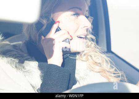 Giovane donna conducente chat sul suo cellulare e guardando fuori della finestra laterale distratti dalla conversazione in una chiave di alta ritratto Foto Stock