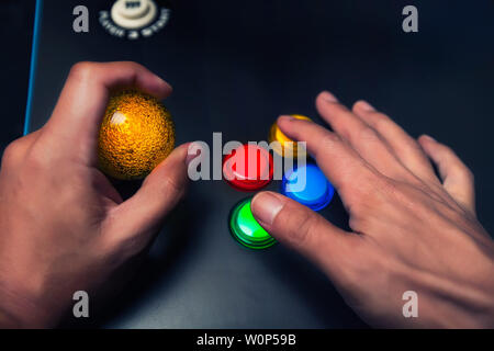 Arcade gamer tenendo una bolla gialla top joystick e giocando su un quattro layout pulsante macchina arcade. Foto Stock