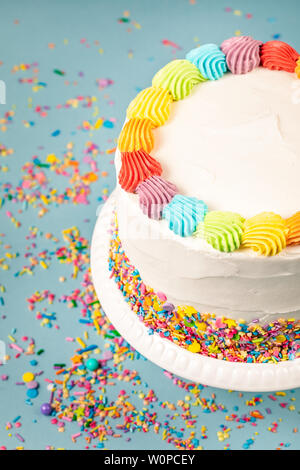 Vista aerea di una torta di compleanno con glassa di arcobaleno colorato e spruzza su uno sfondo blu. Foto Stock