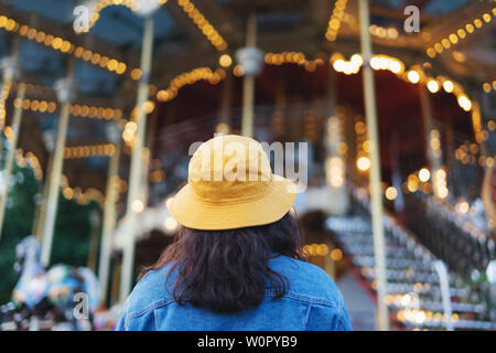 Giovane donna nel cappello giallo guardando alla rotatoria nel parco tematico in estate Foto Stock