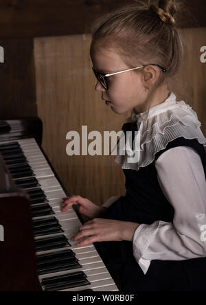 Strict bambina in grandi bicchieri suonare il pianoforte, bambino imita il maestro. Foto Stock