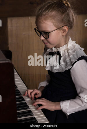 Strict bambina in grandi bicchieri suonare il pianoforte, bambino imita il maestro. Foto Stock