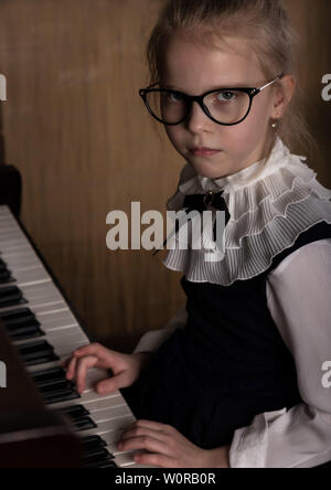 Strict bambina in grandi bicchieri suonare il pianoforte, bambino imita il maestro. Foto Stock