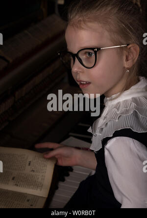 Strict bambina in grandi bicchieri suonare il pianoforte, bambino imita il maestro. Foto Stock