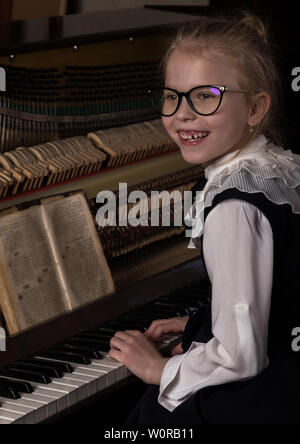 Strict bambina in grandi bicchieri suonare il pianoforte, bambino imita il maestro. Foto Stock