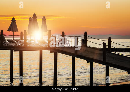 Splendida vista del molo con ombrelloni e sedie a sdraio sul bellissimo tramonto. il cielo è rosso e arancione, il mare è calmo. Concetto di vacanza Foto Stock