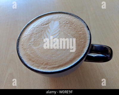 Balck tazza di cappuccino sul piattino con una foglia pattern in schiuma sul tavolo. Foto Stock