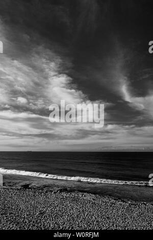 Immagine in bianco e nero di una spiaggia con un solitario petroliera di carbone all'orizzonte al di sotto di un moody cielo molto nuvoloso Foto Stock