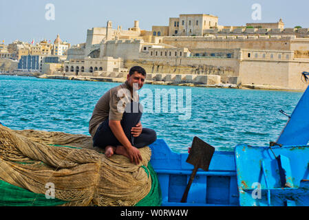 Pescatore seduto su reti da pesca con vista sul Porto Grande di La Valletta, Malta Foto Stock