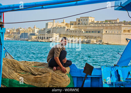 Pescatore seduto su reti da pesca con vista sul Porto Grande di La Valletta, Malta Foto Stock