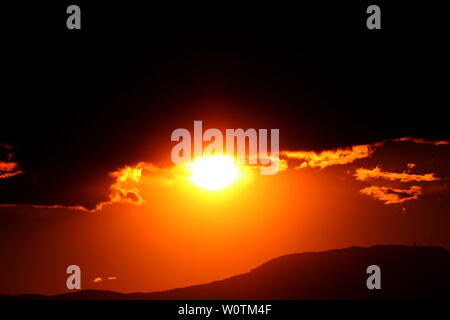 Wie ein Auge wirkt die untergehende Sonne zwischen den Wolken und den Bergen bei Malinska in Kroatien / Hrvatska / Croazia Foto Stock