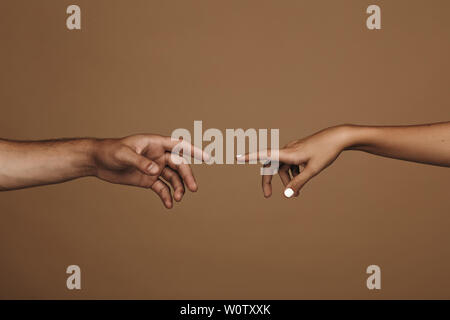 Close up di un uomo e di una donna mano circa a toccare con il dito indice. Matura in amore di raggiungere l'uno all'altro nella parte anteriore di sfondo marrone. Foto Stock