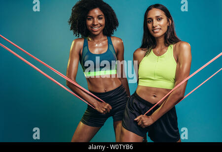 Montare due donne a fare gli esercizi con resistenza band su sfondo blu. Certi giovani femmine fitness lavora con banda di resistenza. Foto Stock