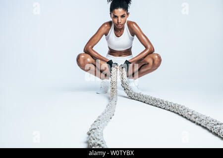 Sudati giovane donna riposo dopo lavoro con funi su sfondo bianco. Femmina africana guardando esausto dopo la formazione incrociata. Foto Stock