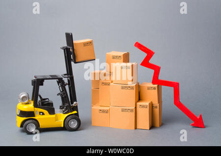 Giallo carrello truckraises una scatola su una pila di scatole e freccia rossa verso il basso. Diminuzione di tariffe economiche per la scarsa domanda di merci, diminuzione di importazione Foto Stock