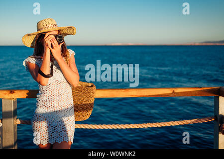 Giovane donna traveler per scattare delle foto del paesaggio di mare sul molo l'utilizzo della fotocamera. Moda estate. La vacanza estiva. Foto Stock