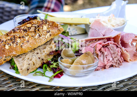 Plowmans pranzo su una piastra bianca con prosciutto e formaggio, coleslaw, sottaceti e pane Foto Stock