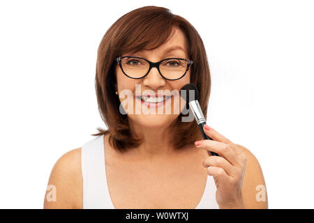 Sorridente donna senior con make up pennello fard Foto Stock